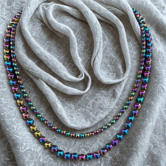 Bohemian Dream Handmade Rainbow Hematite Necklace with iridescent beads laid on textured fabric