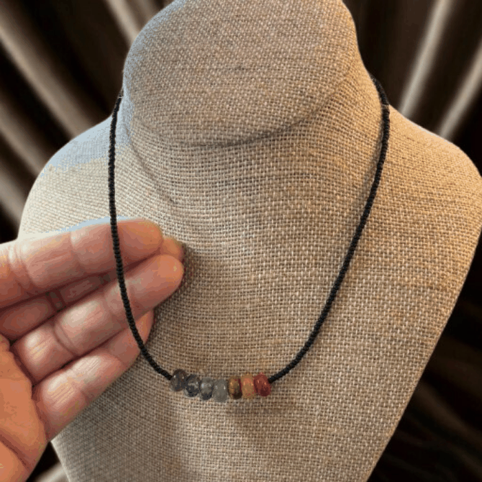 Handcrafted Chakra Necklace with Genuine Gemstones displayed on a bust with a hand holding it