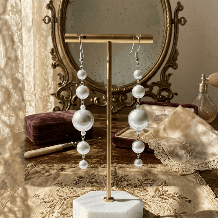 Elegant White Glass Pearl Dangle Earrings displayed on a jewelry stand with vintage decor
