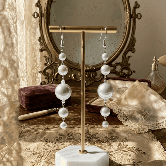 Elegant White Glass Pearl Dangle Earrings displayed on a jewelry stand with vintage decor