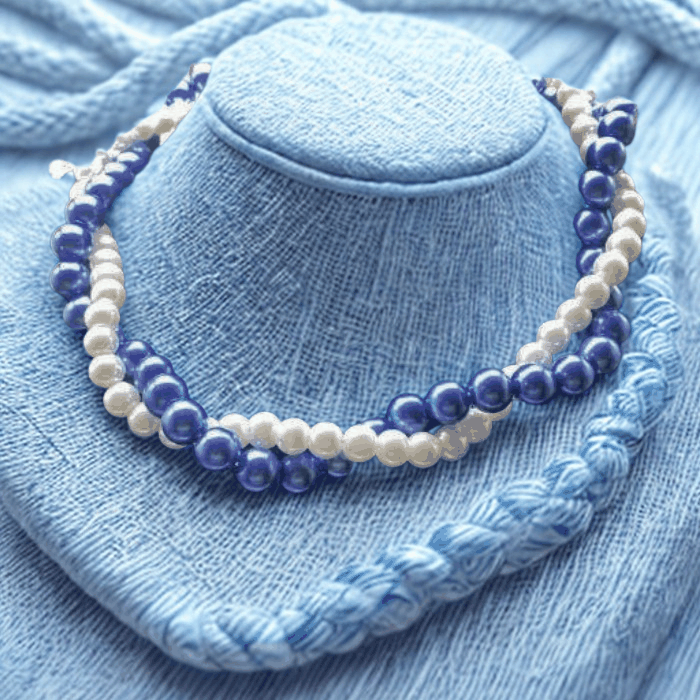 Elegant twisted royal blue and white glass pearl necklace on blue fabric background.