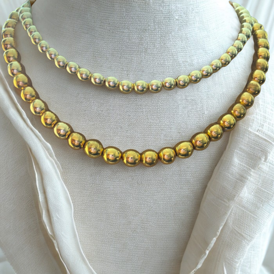 Gold Hematite Gemstone Necklace displayed on white fabric with round shiny gold beads