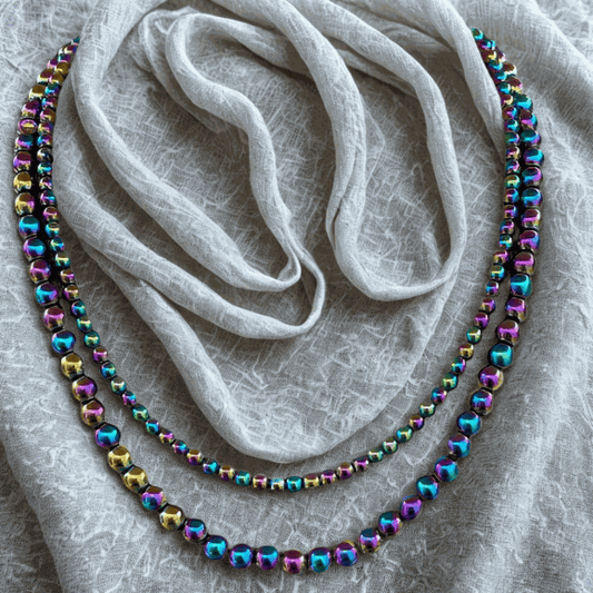 Bohemian Dream Handmade Rainbow Hematite Necklace with iridescent beads laid on textured fabric