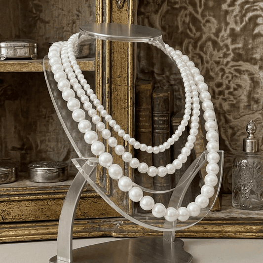 Classic Single Strand White Pearl Necklace displayed on a clear stand with elegant vintage backdrop