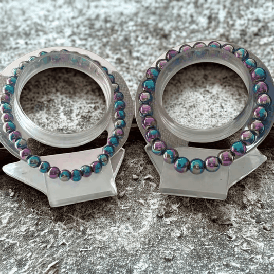 Colorful Rainbow Hematite Bracelet by Peace N Beads displayed on clear stands against textured background