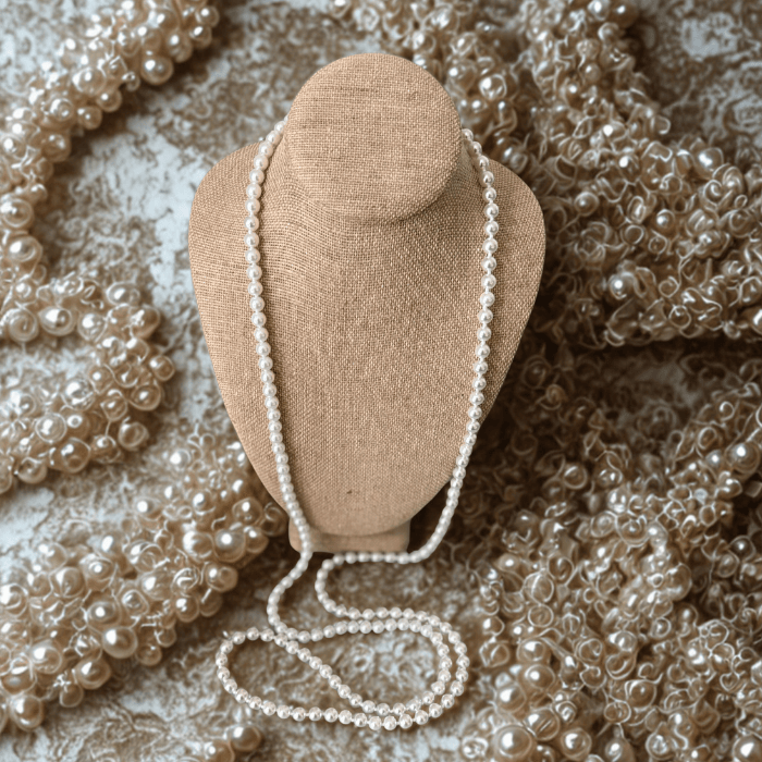 Classic 55 Inch White Glass Pearls Necklace displayed on a beige bust with additional pearls in the background