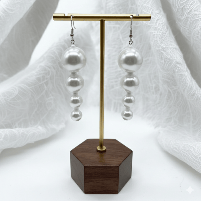 Pearl Perfection White Glass Drop Earrings gracefully displayed on a wooden stand